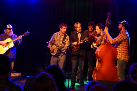 Chris Roszell performing with his bluegrass band under dramatic stage lighting